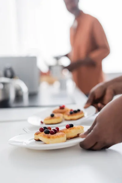 Cropped view of african american woman holding plates with ukrainian pancakes and berries — Stock Photo