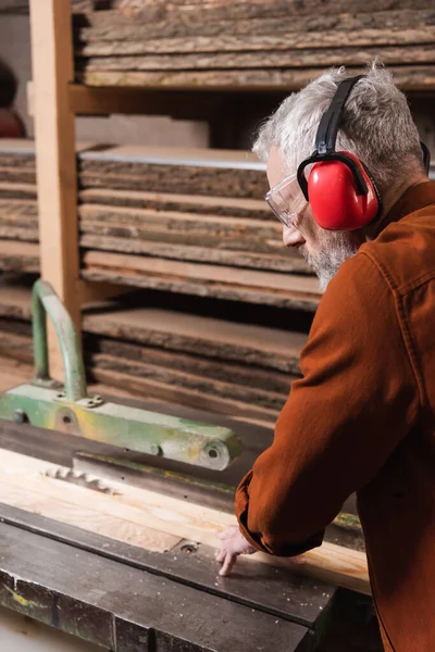 Woodworker in protective earmuffs cutting boards on circular saw — Stock Photo