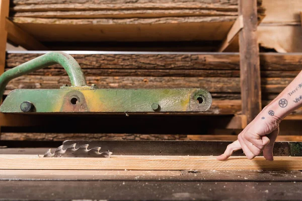Partial view of tattooed woodworker cutting plank on circular saw — Stock Photo