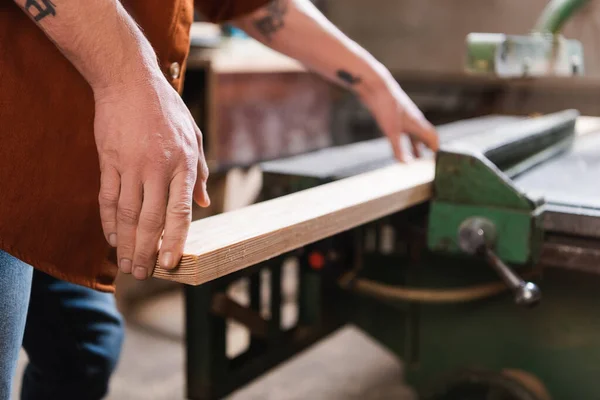 Teilansicht tätowierter Möbeldesigner mit Holzplanke im Holzwerkatelier — Stockfoto