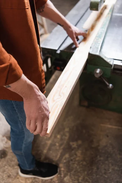 Cropped view of carpenter working with board on jointer machine — Stock Photo
