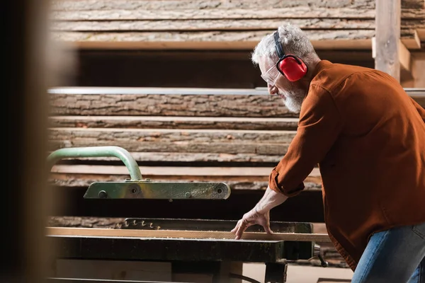 Vue latérale du menuisier mature coupant du bois sur scie circulaire — Photo de stock