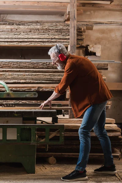 Vue latérale du concepteur de meubles travaillant sur scie circulaire dans l'atelier — Photo de stock