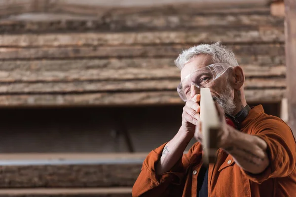 Плотник средних лет проверяет размытую доску в мастерской — стоковое фото