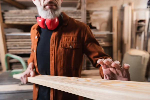 Cropped view of bearded carpenter checking board in woodwork studio — Stock Photo