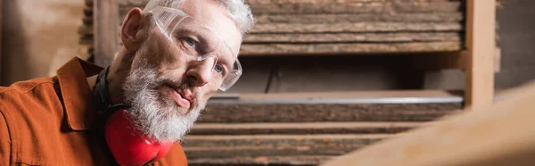 Bearded furniture designer in goggles working in woodwork studio, banner — Stock Photo