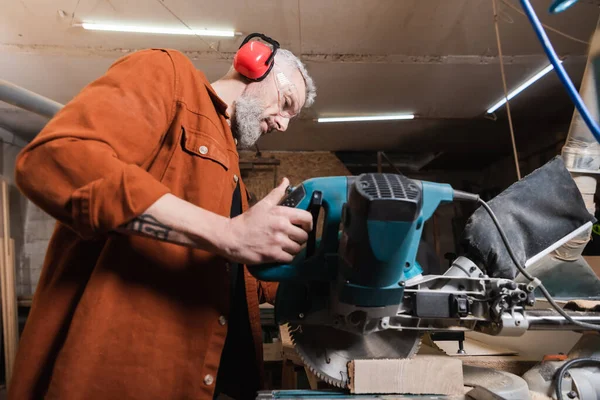 Low angle view of carpenter cutting timber with miter saw — Stock Photo