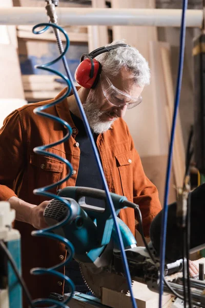 Bearded middle aged carpenter working with miter saw in workshop — Stock Photo