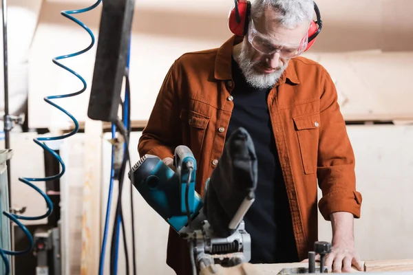 Menuisier mature travaillant avec une scie à onglets dans un atelier de menuiserie — Photo de stock