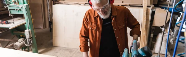 Bearded carpenter in eyeglasses working with miter saw in workshop, banner — Stock Photo