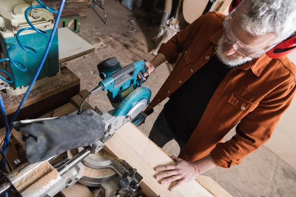 High angle view of mature carpenter cutting board with miter saw — Stock Photo