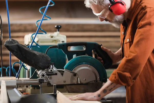 Side view of middle aged carpenter cutting timber on miter saw — Stock Photo