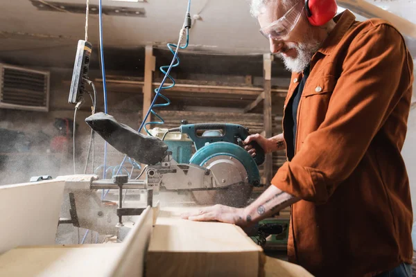 Side view of bearded woodworker cutting board near miter saw — Stock Photo