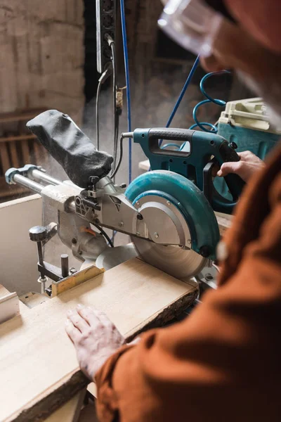 Partial view of blurred woodworker cutting board with miter saw — Stock Photo