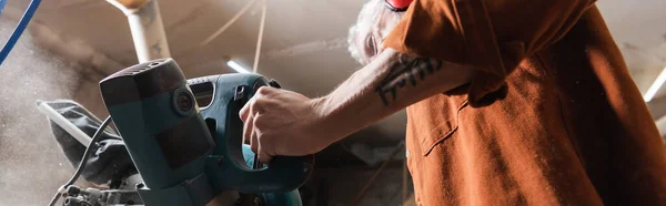 Vista de ángulo bajo de carpintero tatuado trabajando con sierra de inglete en taller, pancarta - foto de stock
