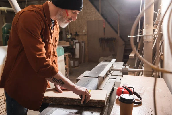 Vue latérale du menuisier en bonnet planche à mesurer près de café à emporter — Photo de stock