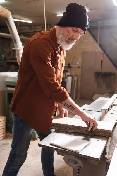 Charpentier tatoué en bonnet planche à mesurer en atelier — Photo de stock