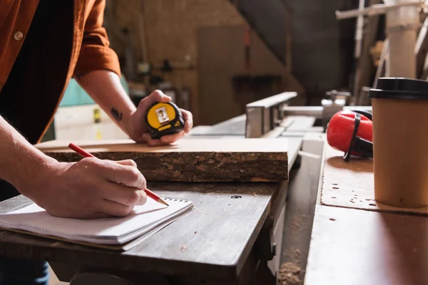 Cropped view of furniture designer holding tape measure and writing in notebook — Stock Photo