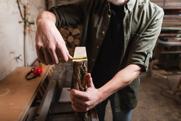 Cropped view of woodworker measuring board with tape measure — Stock Photo