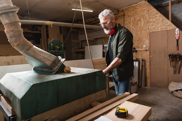 Carpintero de pelo gris que trabaja cerca de la campana de ventilación en un estudio de carpintería - foto de stock