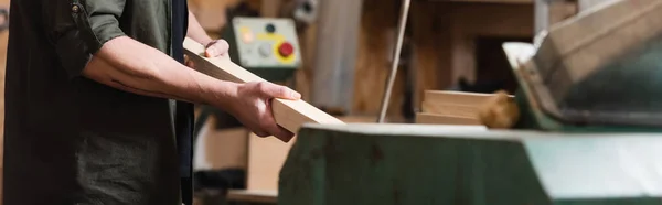 Vista recortada del diseñador de muebles sosteniendo tablón de madera en el estudio de carpintería, pancarta - foto de stock