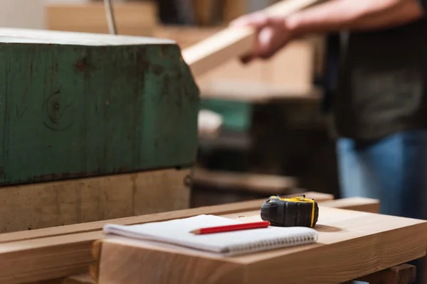 Selective focus of notebook, pencil and tape measure near cropped carpenter on blurred background — Stock Photo