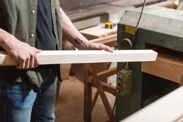 Cropped view of joiner holding wooden plank near thickness planer — Stock Photo