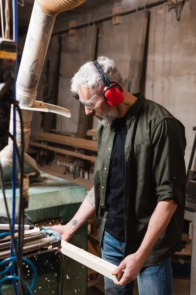 Falegname maturo in maschera che lavora con tavola di legno in officina — Foto stock