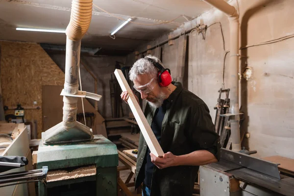 Menuisier en lunettes et cache-oreilles protecteurs panneau de contrôle en atelier — Photo de stock