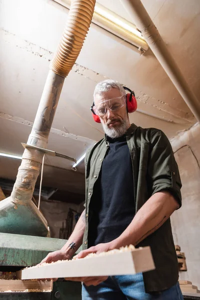 Vue à angle bas du charpentier barbu tenant une planche en bois dans l'atelier — Photo de stock