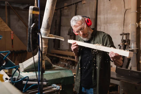 Mature woodworker blowing sawdust off plank in carpentry studio — Stock Photo