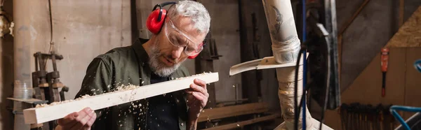 Woodworker in goggles blowing sawdust from plank, banner — Stock Photo