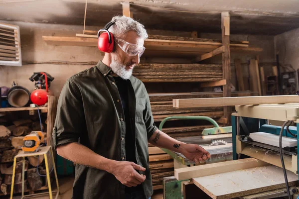 Grey haired carpenter working near thickness planer in workshop — Stock Photo