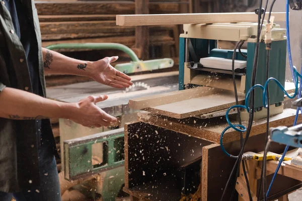 Partial view of tattooed furniture designer pointing at boards in thickness planer — Stock Photo