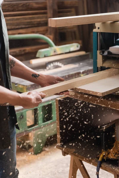 Cropped view of tattooed carpenter working on bench thicknesser in workshop — Stock Photo