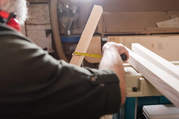 Partial view of blurred furniture designer measuring wooden plank — Stock Photo