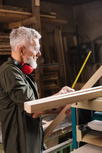 Side view of bearded woodworker measuring board in workshop — Stock Photo