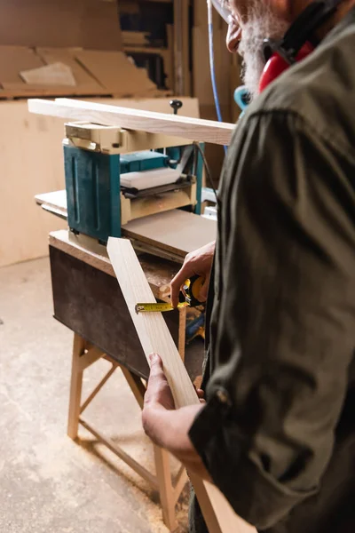 Partial view of woodworker measuring plank near thickness planer — Stock Photo