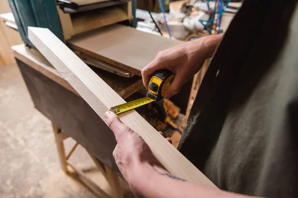 Cropped view of furniture designer measuring plank while working in woodwork studio — Stock Photo