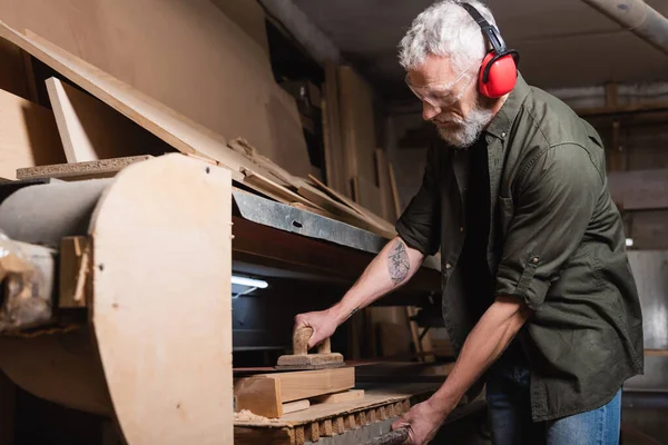 Bearded woodworker polishing board in sander machine — Stock Photo