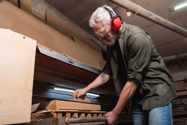 Woodworker in earmuffs polishing timber in sander machine — Stock Photo