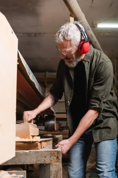Bearded carpenter in goggles polishing board in sander machine — Stock Photo