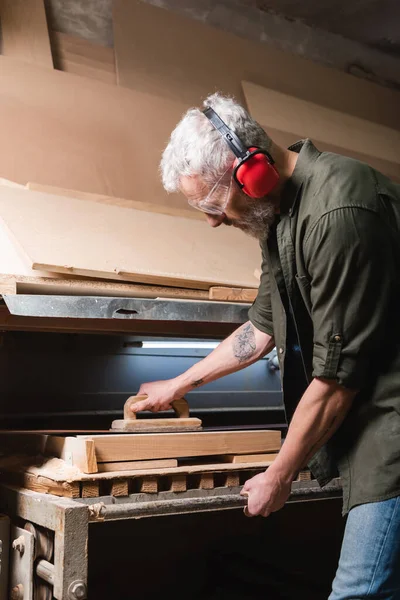 Side view of grey haired carpenter polishing board in sander machine — Stock Photo