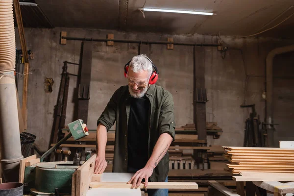Glücklicher Tischler mittleren Alters, der in der Werkstatt an einer Schreinermaschine arbeitet — Stockfoto