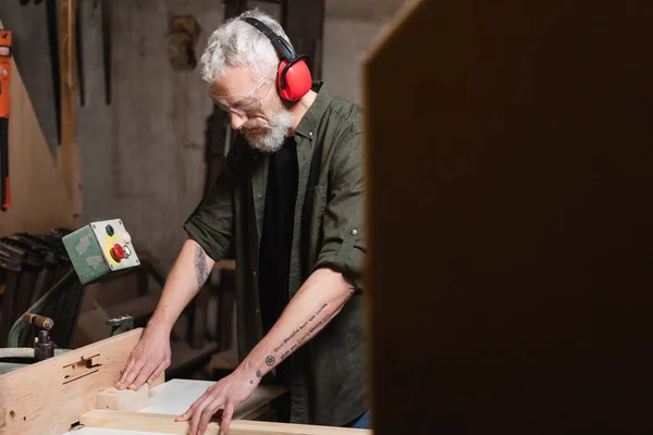 Carpinteiro tatuado trabalhando na máquina jointer em primeiro plano desfocado — Fotografia de Stock