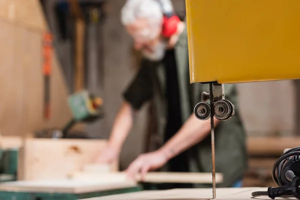 Selective focus of band saw near carpenter working on blurred background — Stock Photo