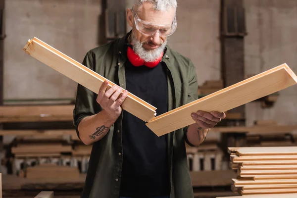 Tattooed furniture designer holding wooden details in woodwork studio — Stock Photo