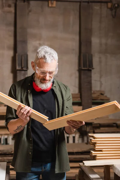 Designer di mobili dai capelli grigi con tavole di legno in falegnameria — Foto stock