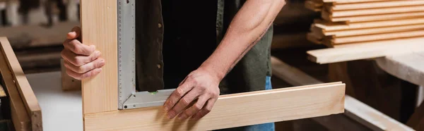 Vista parcial del diseñador de muebles que mide los detalles de madera con regla de esquina, bandera - foto de stock