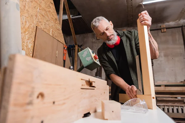 Бородатый дизайнер мебели, измеряющий деревянный угол на размытом переднем плане — стоковое фото